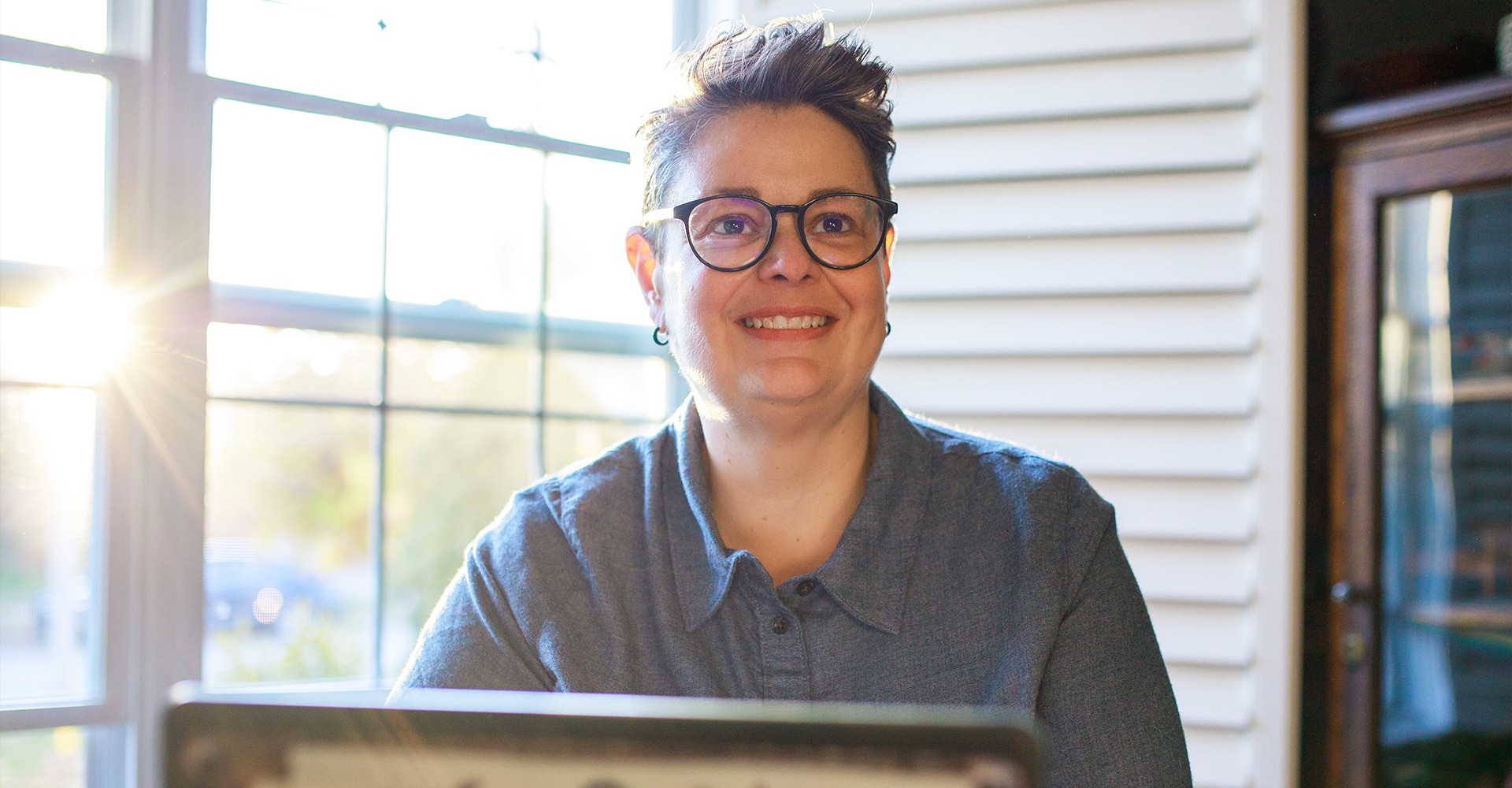 A photographic style image of Melisse sitting behind her desk while looking into the camera and smiling.